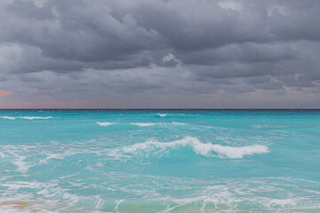 Fototapeta premium A powerful landscape showing the intense blue of the Caribbean Sea with white-capped waves under a heavy, overcast grey sky in Cancun.
