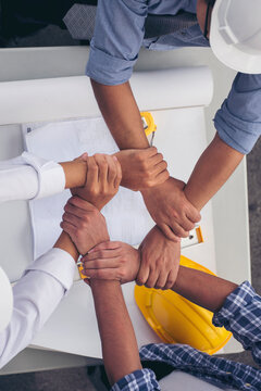 Vertical close-up construction engineer man hands working at office desk architect workplace. Multiracial people fist bump partner colleague logistics Warehouse. Hardhat Protect Civil Construction.