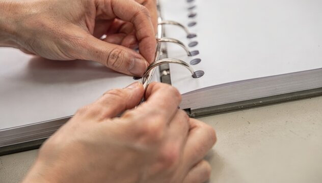 Closeup shot of hands punching pages and threading twinloop wire through holes creating durable layflat books with precise wirebound binding technique.