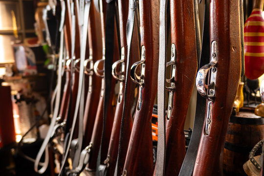 Row of Antique Wooden Rifles With Leather Slings Displayed in Shop.
