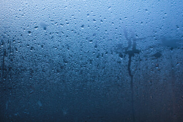 Abstract background of natural water condensation on window glass with blue gradient light. Rain drops and steam texture on transparent surface, perfect for weather, freshness, or moody concepts. © Eko Sasmito