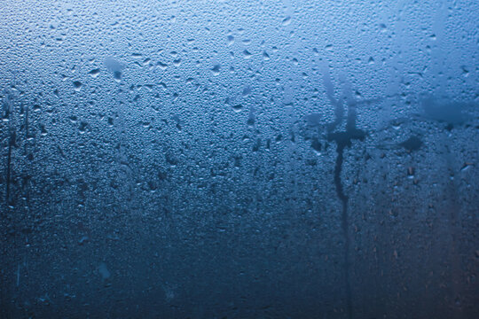Abstract background of natural water condensation on window glass with blue gradient light. Rain drops and steam texture on transparent surface, perfect for weather, freshness, or moody concepts.