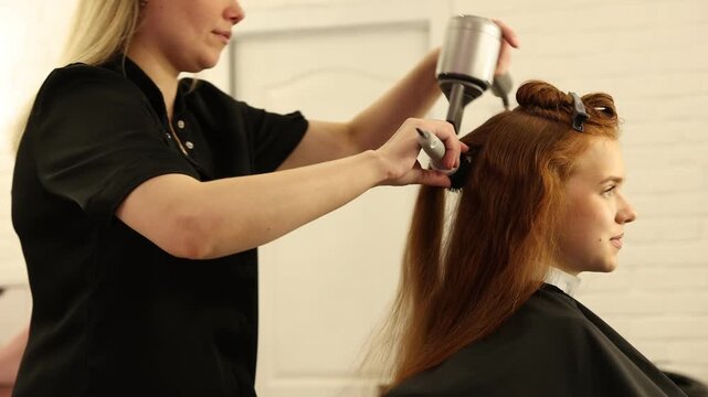 Stylist blow drying girl's hair in beauty salon