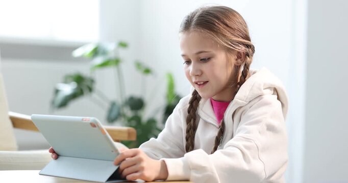 Little girl using modern tablet at wooden table indoors