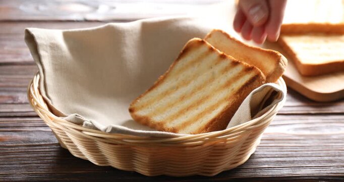 Woman putting browned toast bread slice into wicker basket at wooden table, closeup