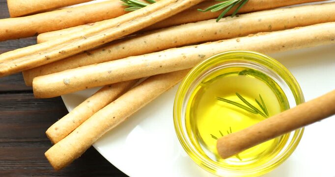 Woman dipping grissini breadstick into oil at wooden table, top view