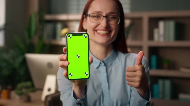 Happy Caucasian business woman show like pointing smartphone green screen inside office smiling female businesswoman thumb up consumer buyer mobile phone mockup chroma key recommending online shopping