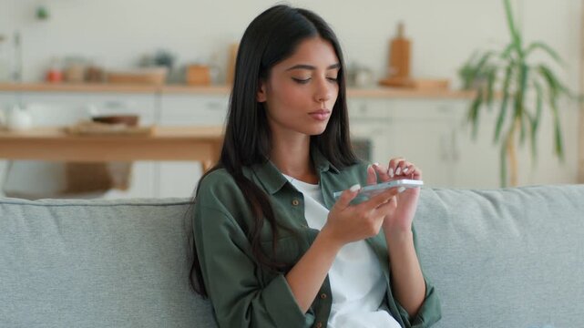 Serious calm Indian Muslim woman recording voice message on cellphone at home using microphone mobile phone loudspeaker dictating SMS audio Arabian female girl talking telephone sending sound indoors