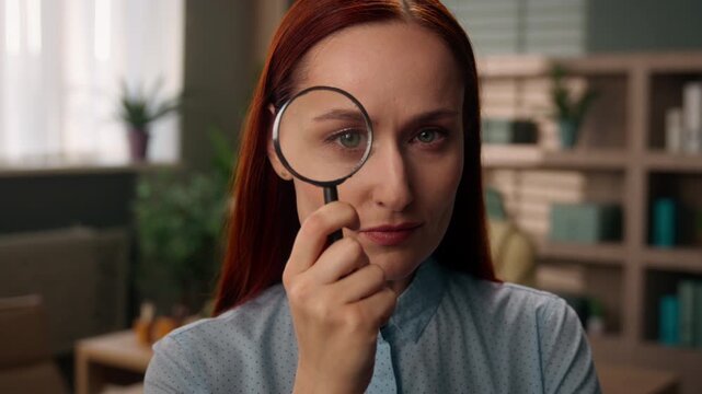 Serious Caucasian business woman looking through magnifying glass examining eye indoor office curious female manager investigating searching analyzing clue businesswoman employer girl research vision
