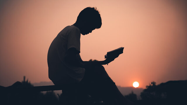 Human holding and reading Bible with light sunset background, christian silhouette concept.
