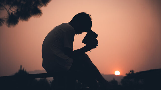 Human holding Bible and praying with light sunset background, christian silhouette concept.