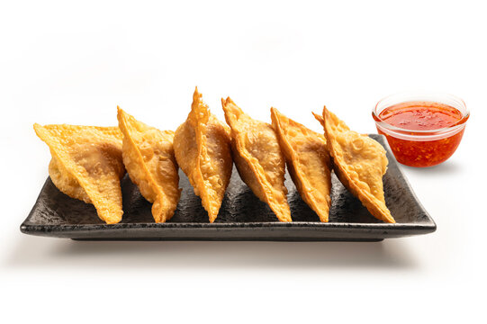 Crispy golden-brown fried wontons on black ceramic plate. Delicious Asian appetizer served with  side of spicy sweet chili dipping sauce on white background.