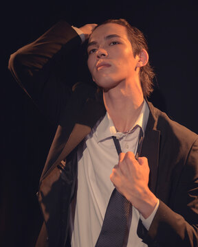 A striking image of a young man adjusting his tie in a dramatic pose that conveys confidence and an air of mystery, with a focus on his intense expression and stylish outfit.