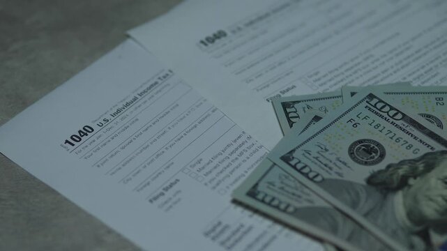 Bundles of hundred dollar bills falling onto the US Individual Income Tax Return form 1040. Video symbolizing tax payment process, tax refund or high income level