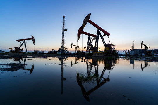 in the evening, oil pumps are running, The oil pump and the beautiful sunset reflected in the water, the silhouette of the beam pumping unit in the evening.