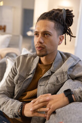 Fototapeta premium Man sitting, leaning forward and clasping hands on gray sofa, wearing denim jacket, smartwatch