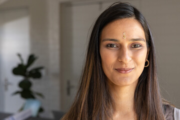 Adult Indian woman making eye contact at home, showing neutral top, forehead jewel and gold hoop © wavebreak3