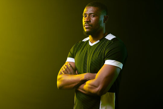 African American man posing with arms crossed in studio wearing black jersey white trim, lighting