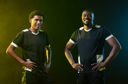 African men teammates posing in studio wearing dark soccer jerseys with white trim and rim haze