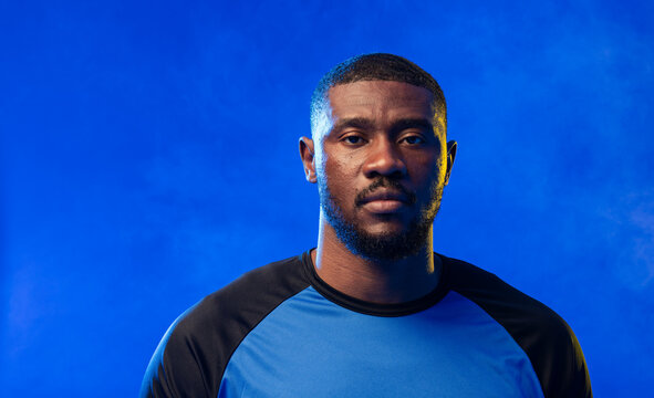 Mid adult African man posing in studio, wearing blue athletic shirt with black raglan sleeves