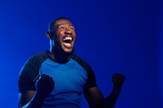 African man shouting and clenching fists while looking upward in studio with blue raglan T-shirt