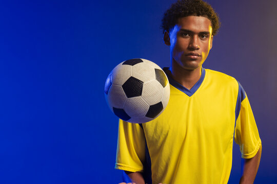 African American male balancing soccer ball at chest, posing in studio lighting with yellow jersey