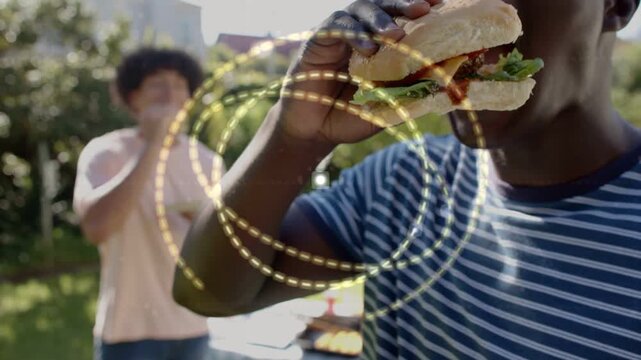 Striped-shirt man eating sandwich at cookout as camera moving in, gold circles expanding over man