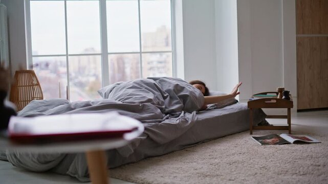 Morning lady checking time cellphone covering blanket continue napping in bed