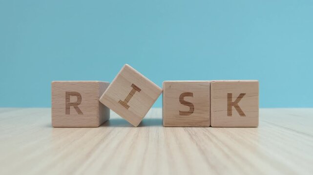 Hand sliding wooden block with the letter K to finish the word RISK on a table with a blue background. Concept of risk assessment, business strategy, and financial management