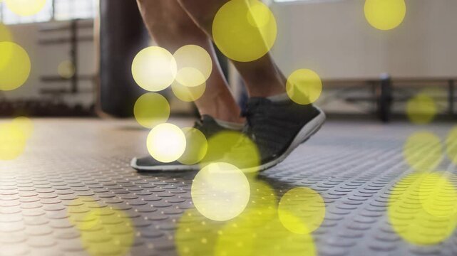 Male athlete starting hop, doing rapid cardio footwork in gym, yellow bokeh drifting across feet