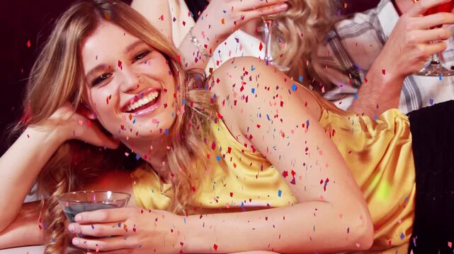 Three friends raising glasses sparking confetti, reclining woman smiling celebrating nightlife