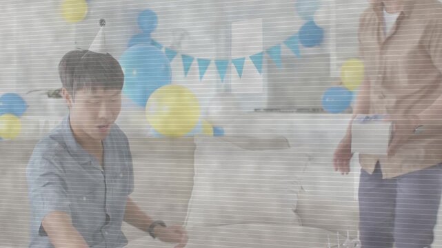 Son adjusting glasses on sofa as father returning with gift box, encouraging birthday with balloons