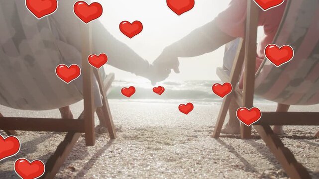 Senior couple reaching hands on beach as red hearts floating forward expressing love for travel