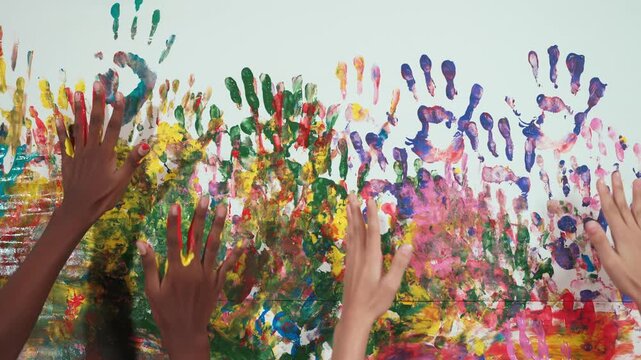 Diverse student hand placed on colorful stained wall while switch place. Closeup of hand or children with mixed races paint their hand print and moving. Background. Creative activity. Edification