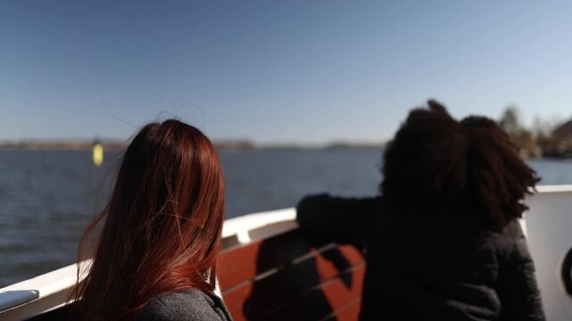 Two young women brunette and afro hair sailing on boat with wind blowing hair creating freedom travel friendship mood on open sea