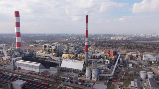 Aerial View Warszawa Power Plant Industrial Complex With Red White Chimneys, Rail Freight, Storage Tanks And Distant City Skyline Under Overcast Sky, Atmospheric Infrastructure Study