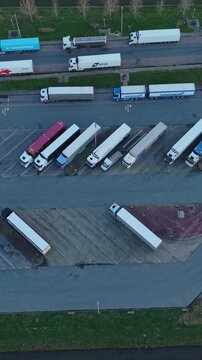 Vertical screen Aerial View Trucks Lined Along Road Convoy Waiting At Staging Terminal, Drivers Taking Breaks, Maintenance Crew Checking Trailers, Planners Reviewing Route Maps, Soft Evening