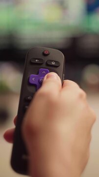 Person using a smart tv remote control for navigating the streaming service menu, changing channels and browsing multimedia content, close up of a hand pressing buttons