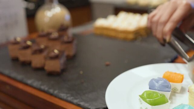 Hand Using Tongs to Pick Chocolate Mousse Cake from Buffet Platter
