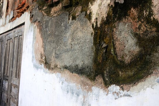 The old building walls with peeling paint and plaster that has crumbled due to high humidity