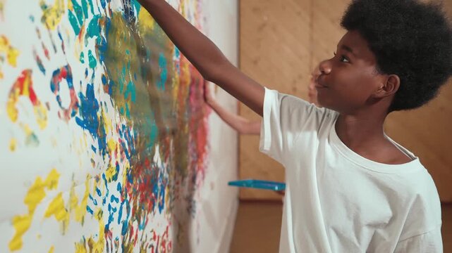 Site view of young diverse children paint colorful stained wall with hand. Attractive high school student paint the wall with hand print while holding color palette. Creative activity. Edification