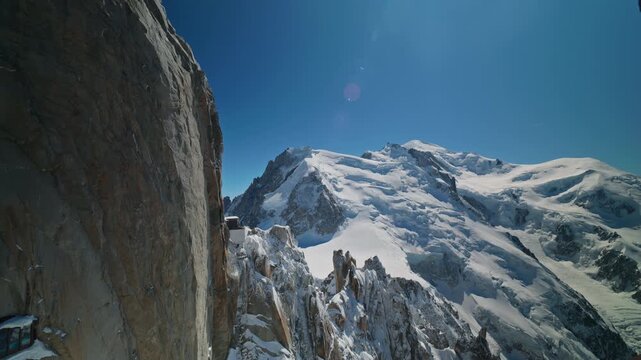 A dramatic composition frames the sheer granite wall of the Aiguille du Midi beside a tiny mountain refuge perched on the rock with the vast glacial face of Mont Blanc rising beyond in Chamonix.