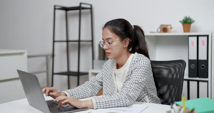 asian entrepreneur sitting focused typing on laptop at home office desk in professional environment performing business task with confident posture and planning mindset