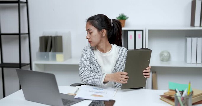 Asian woman opening brown folder and preparing documents while seated at tidy home desk working with concentration in calm modern office during peaceful work from home day