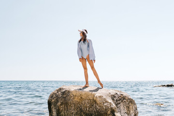 Woman Sea Rock: Young woman in swimwear stands on large boulder in clear sea, enjoying sunny summer leisure. © svetograph