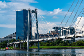 Fototapeta premium Modern Cable-Stayed Pedestrian Bridge Over River With City Skyline and Glass Office Tower