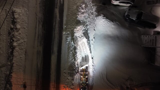 Cinematic aerial drone shot of a snowplow working on snow-covered streets in Beechville near Halifax after heavy snowfall. Nova Scotia, Canada, nighttime road clearing in suburban area 4K.