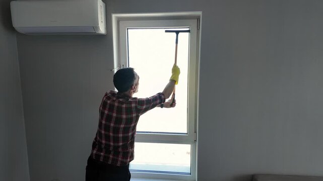 A man washes the windows of a modern apartment using a squeegee