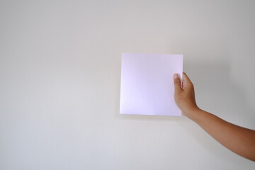 Obraz premium Holding a Blank Square of Paper Against a White Wall