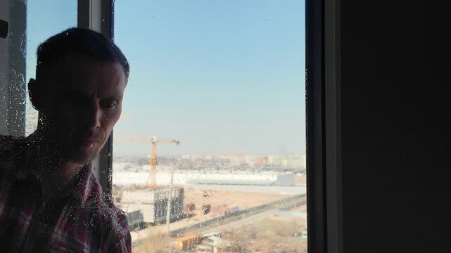 A frontal view from behind the glass shows a cleaner in yellow rubber gloves carefully cleaning a dirty window with a sponge. Cleaning services and professional house cleaning